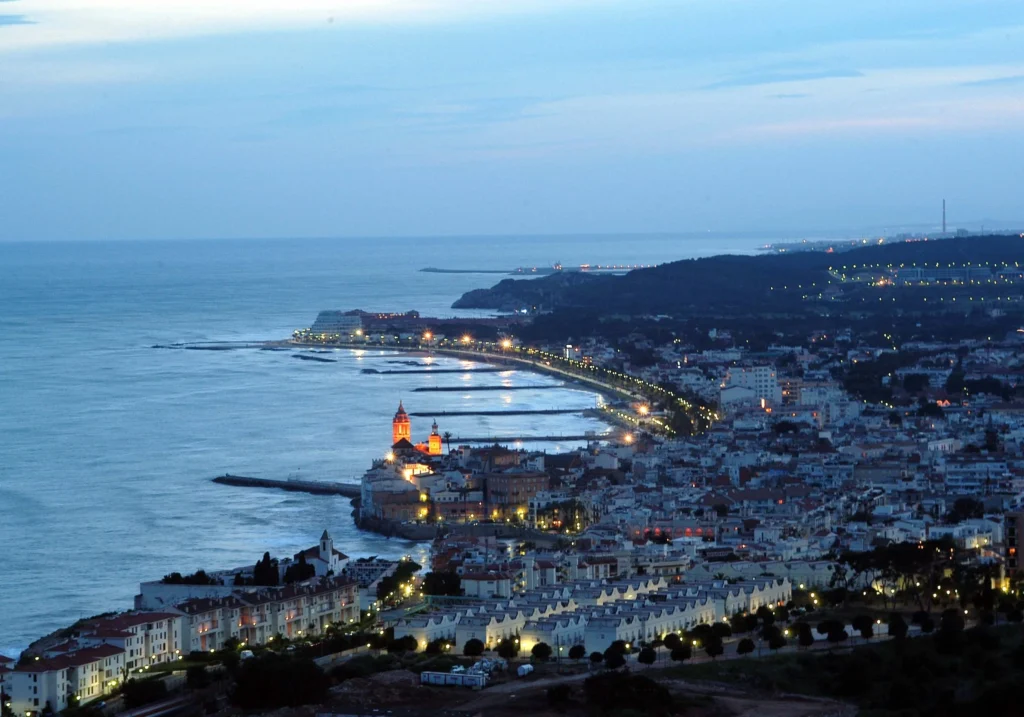 Vista nocturna de Sitges il·luminada des d'un turó, amb el mar al fons