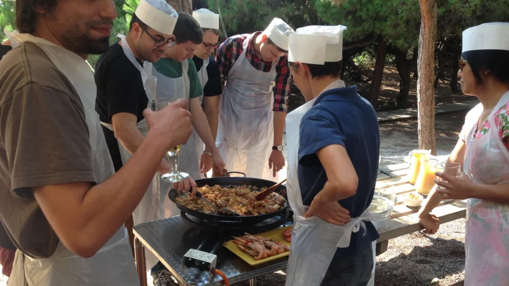 Grup amb barrets de cuiner preparant una paella a l'aire lliure com a activitat de team building
