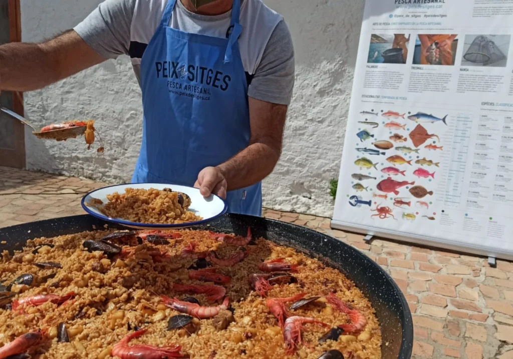 Cuiner de Peix Sitges servint una paella de marisc en una paellera gran